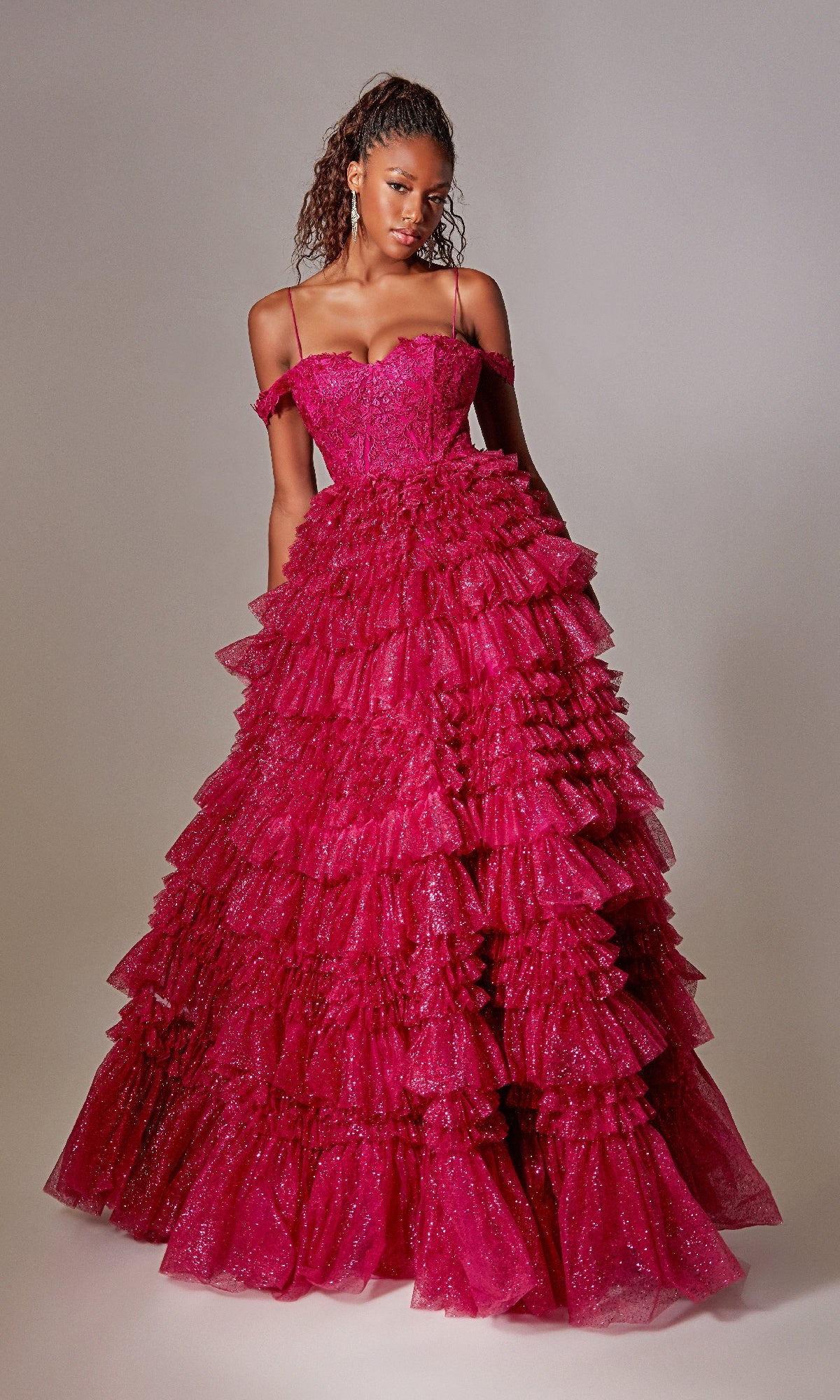 A woman stands against a plain background wearing the Raspberry Pink Long Glitter Prom Dress with ruffles, featuring multiple layers of ruffled tulle and thin straps.